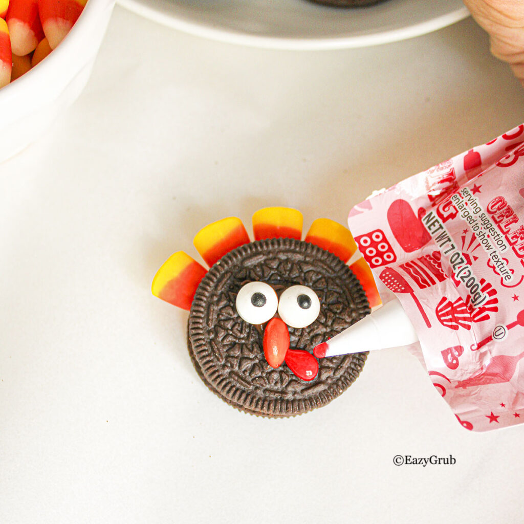 A red turkey waddle is piped on using red cookie icing making it look like turkey oreos.