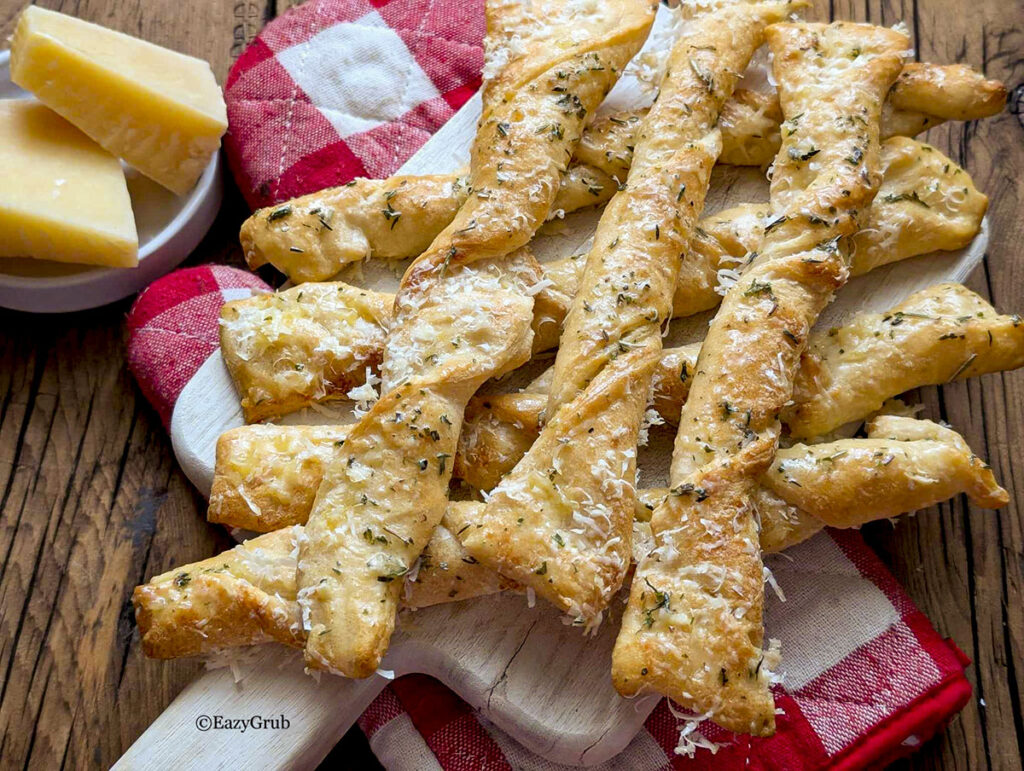 Garlic twists on a wooden board with a red and white checked oven mitt underneath.