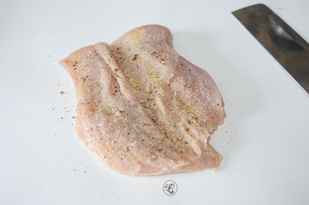 A chicken breast cut in half horizontally and seasoned.