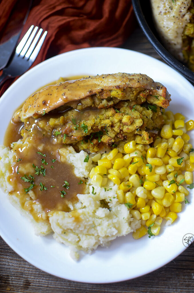 stuffed chicken breast with corn and potatoes on a white plate.