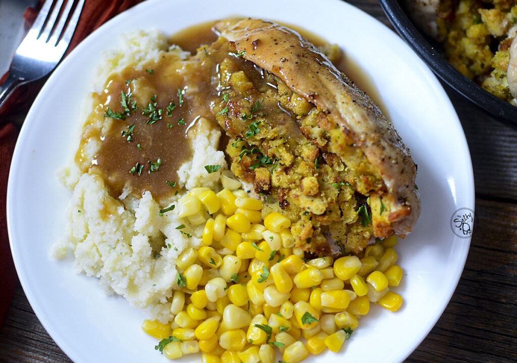 Stuffed chicken breast on a white plate with corn, mashed potatoes and gravy.