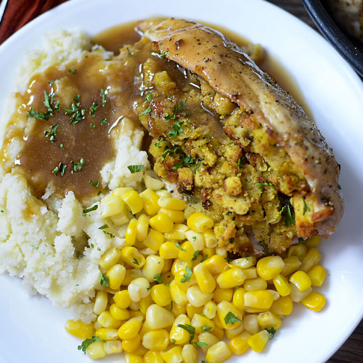 Stuffed chicken breast on a white plate with corn, mashed potatoes and gravy.