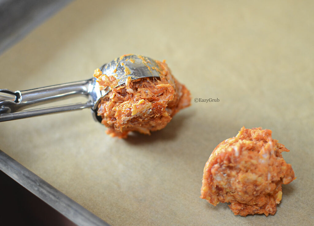 Chorizo balls (raw) on a baking sheet with a cookie scoop.