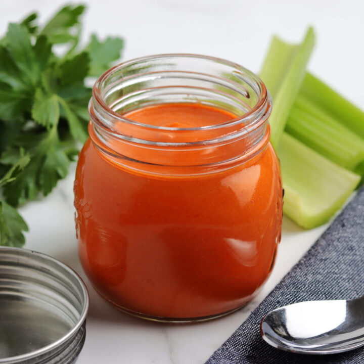 Homemade buffalo sauce in a clear glass jar, vibrant orange-red in color with a smooth, creamy texture.