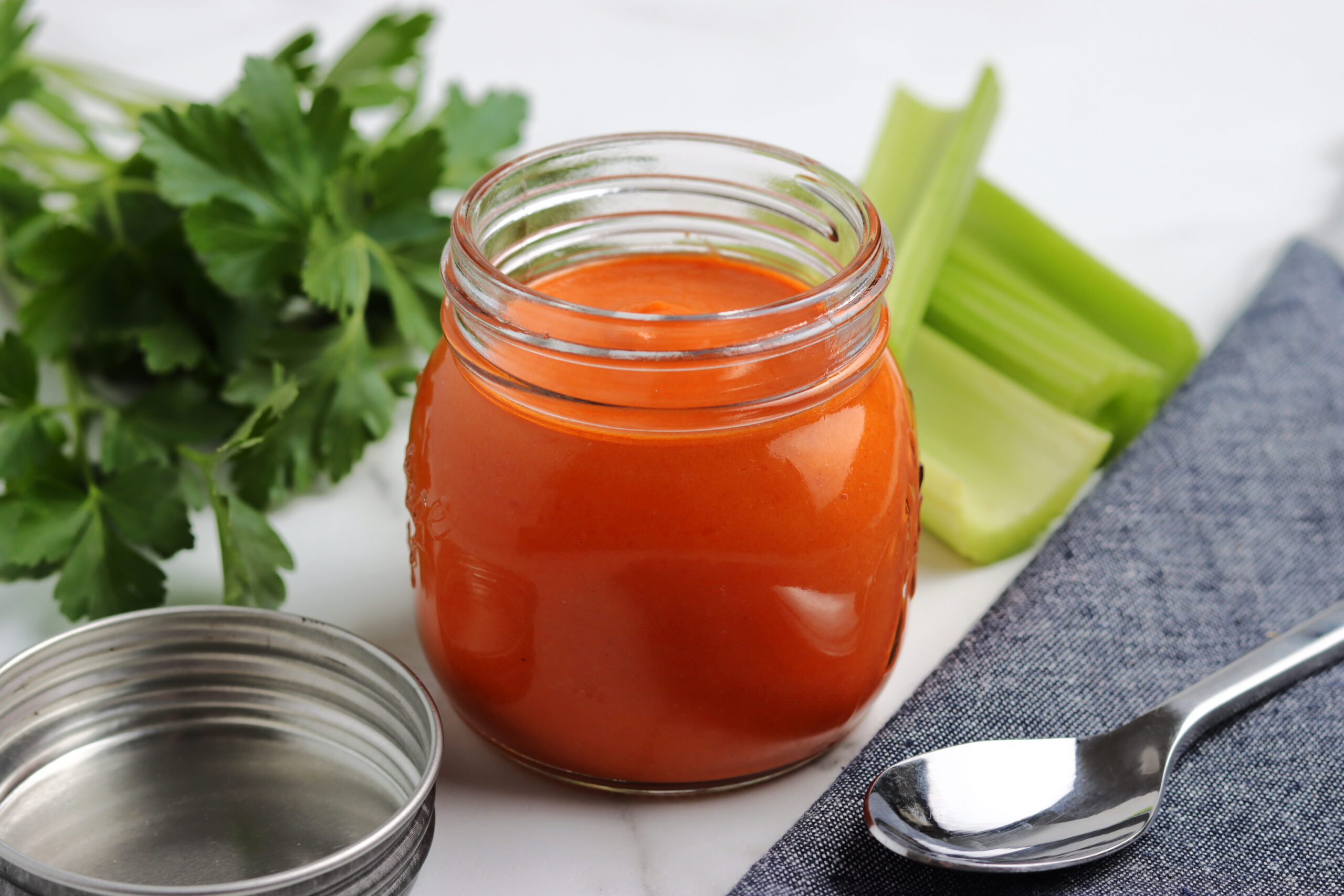 Homemade buffalo sauce in a clear glass jar, vibrant orange-red in color with a smooth, creamy texture.