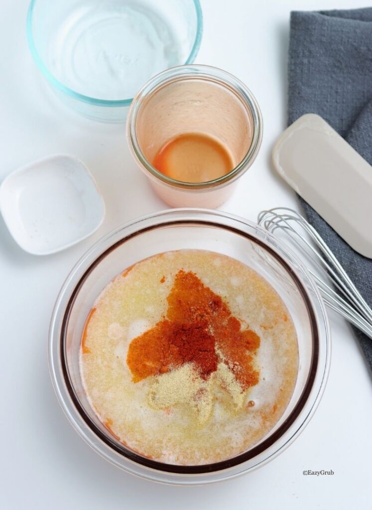 Hot sauce, melted butter, and spices in a mixing bowl before whisking.