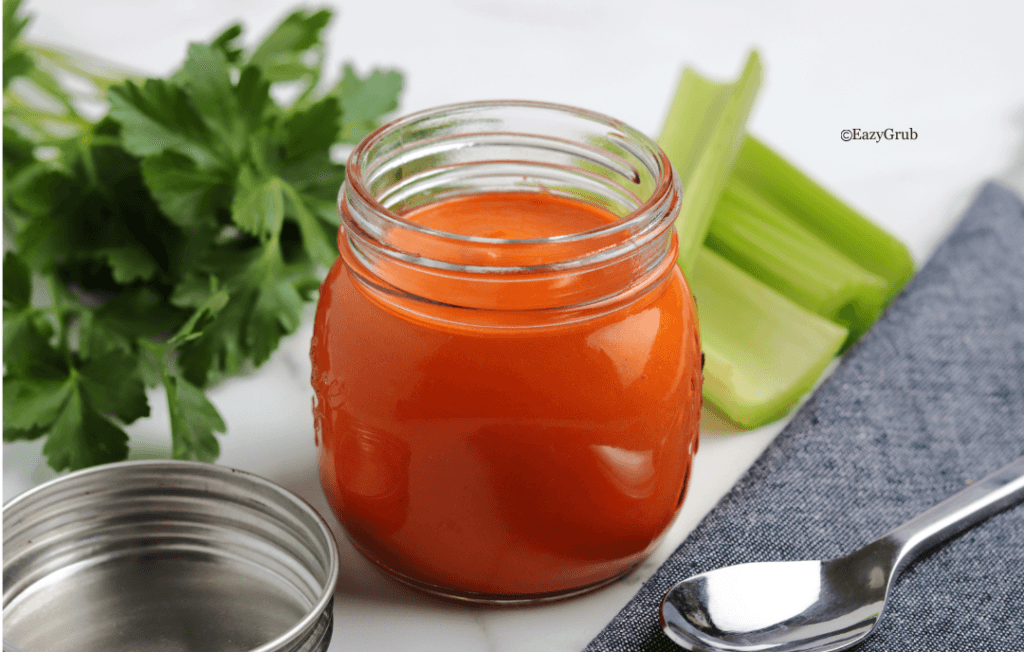 Homemade buffalo sauce in a clear glass jar, vibrant orange-red in color with a smooth, creamy texture.