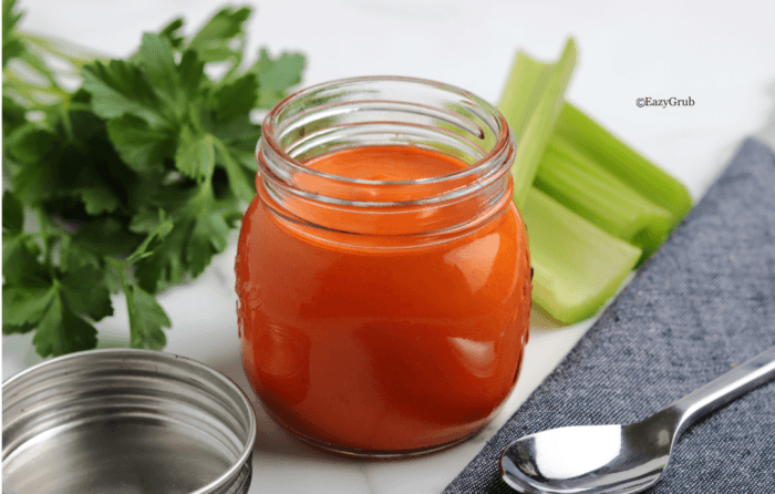 Homemade buffalo sauce in a clear glass jar, vibrant orange-red in color with a smooth, creamy texture.