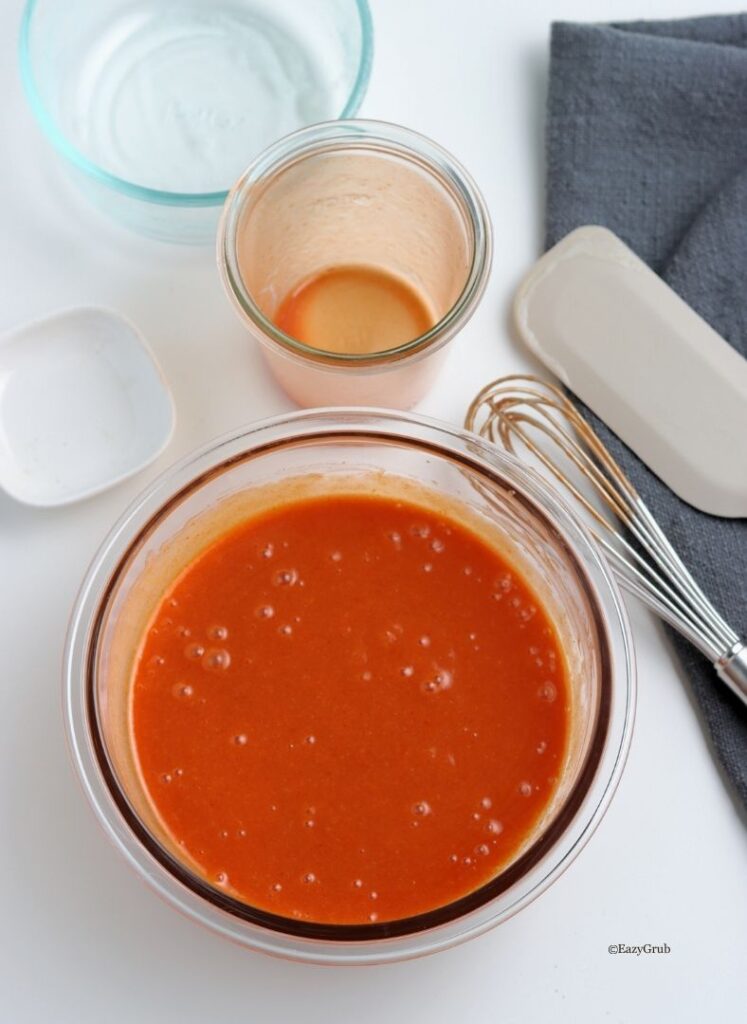 Buffalo sauce being whisked in a bowl until smooth and emulsified.