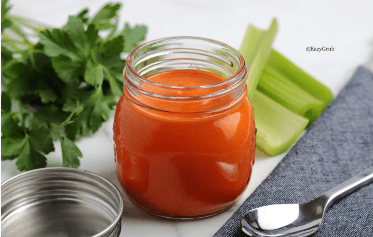 Homemade buffalo sauce in a clear glass jar, vibrant orange-red in color with a smooth, creamy texture.
