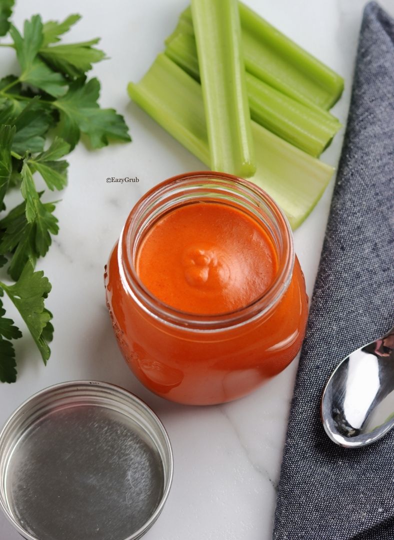 Homemade buffalo sauce in a clear glass jar, vibrant orange-red in color with a smooth, creamy texture.