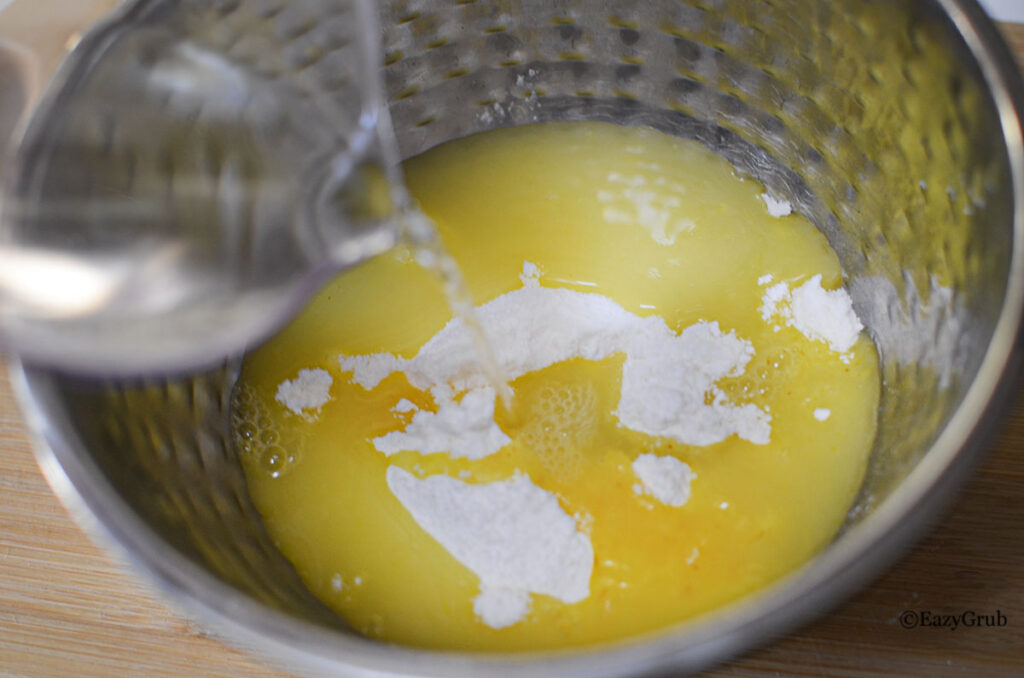 Instant lemon pudding mix being whisked with hot water in a mixing bowl.