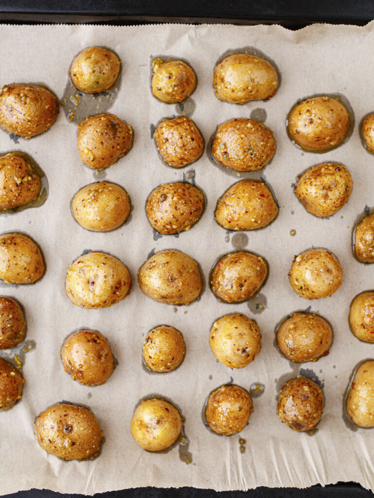 Seasoned baby potatoes arranged cut side down on a parchment lined baking dish.
