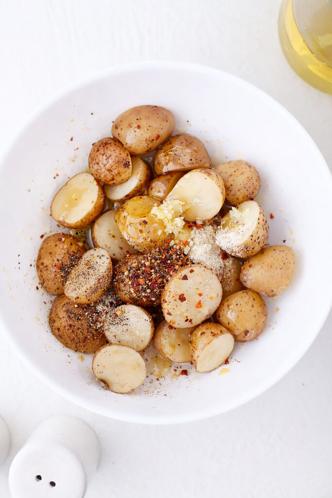 Baby potatoes in a white bowl with seasonings on top.