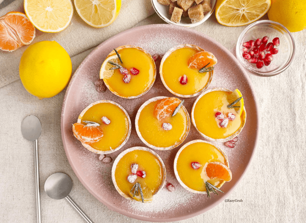 Finished lemon curd tarts arranged on a serving platter, bright yellow filling with rosemary, tangerina and pomegranate