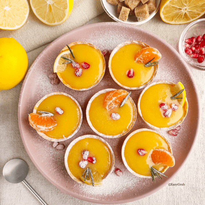 Finished lemon curd tarts arranged on a serving platter, bright yellow filling with rosemary, tangerina and pomegranate