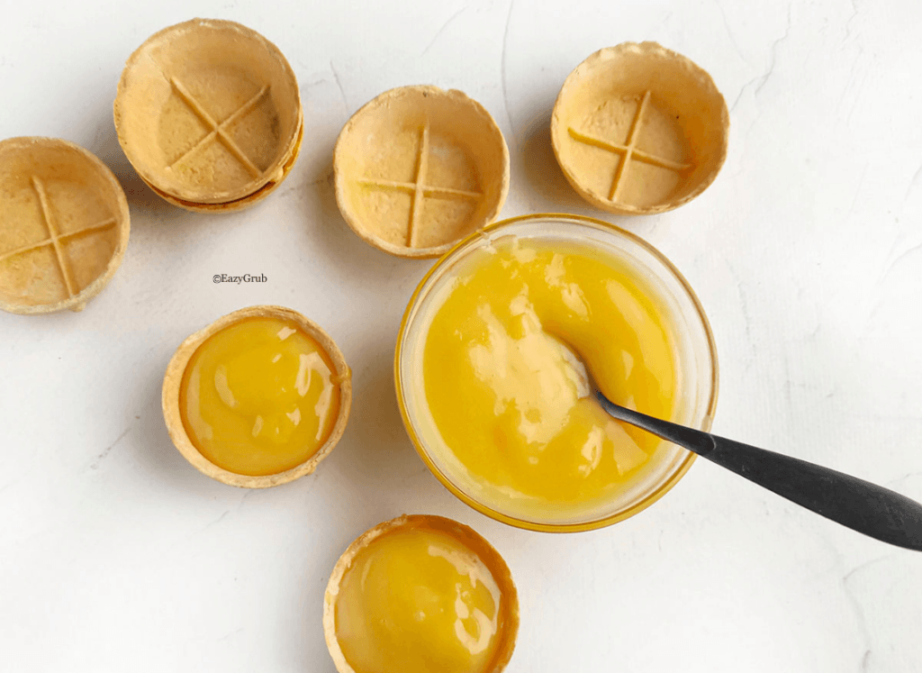Lemon curd being spooned into mini tart shells for quick 2-ingredient lemon curd tarts.