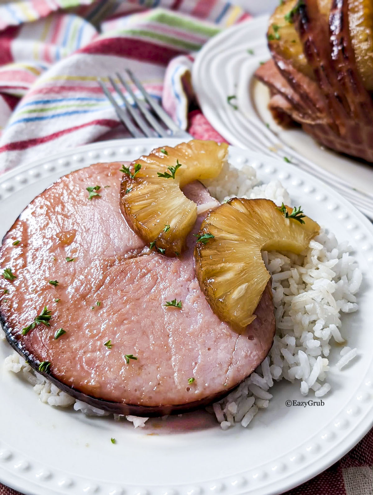 A slice of boneless ham resting on a white plate with a roasted pineapple ring sitting on top (in half).