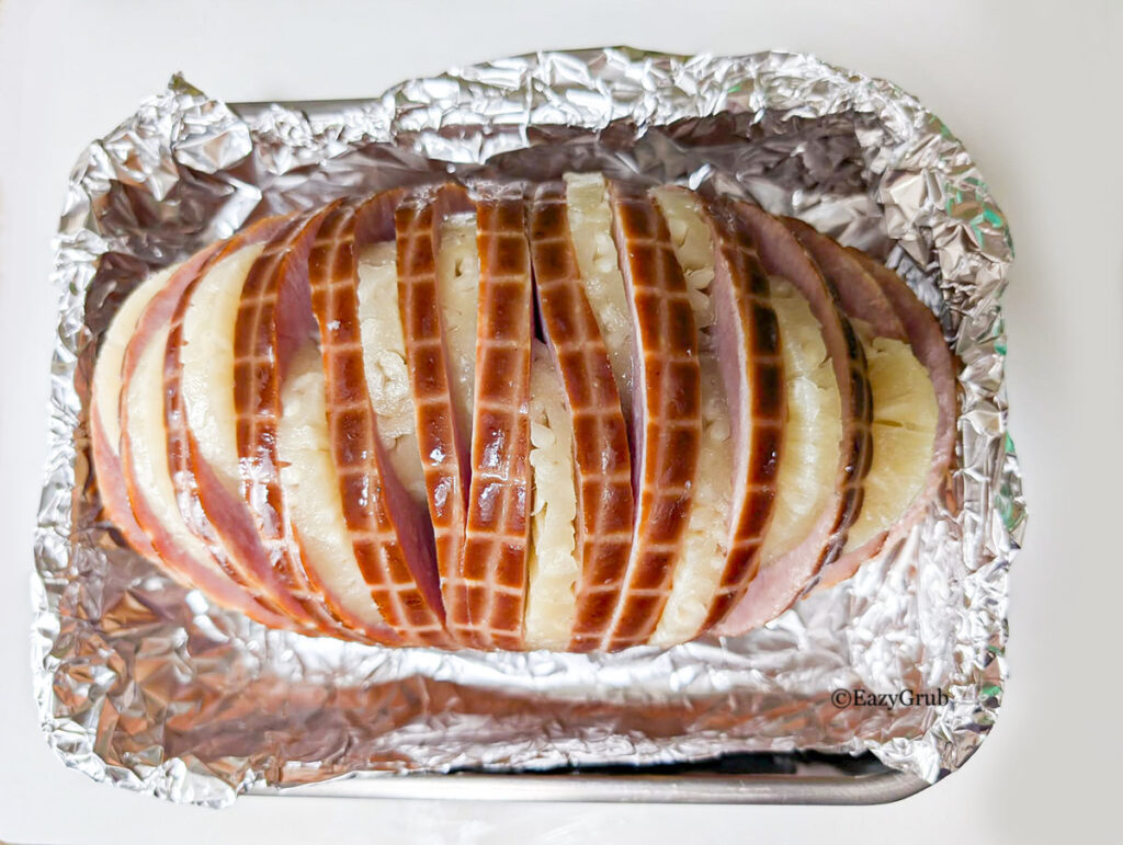 the boneless ham sliced with pineapple rings in each slice in a roasting pan lined with foil.