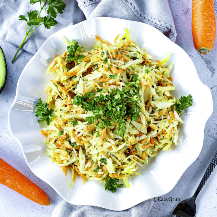 Avocado Coleslaw in a white bowl with carrots around it on the table. Featured Image.
