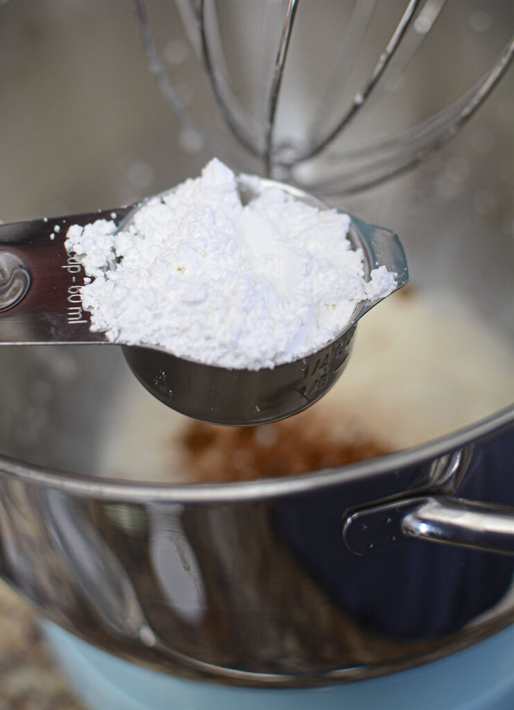 Powdered sugar in a measuring cup about to be poured into the mixing bowl.