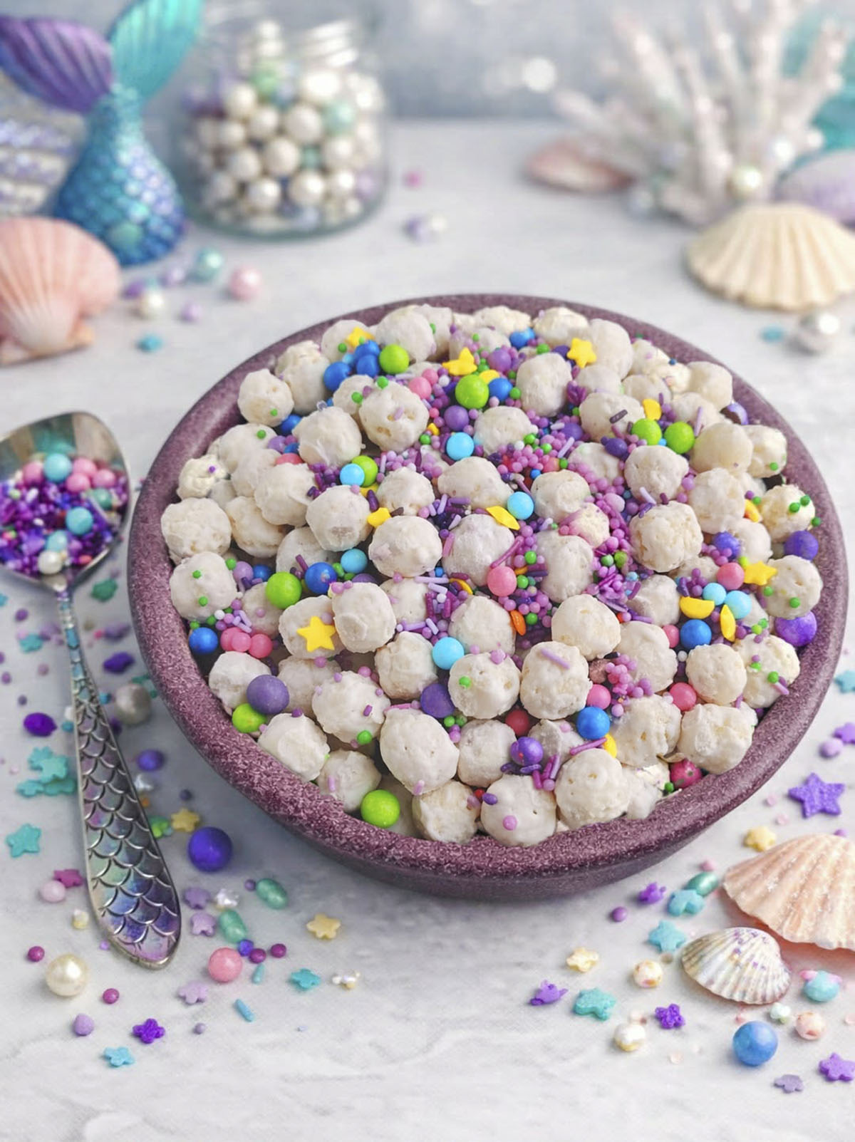 Mermaid poop treat in a bowl with a pretty spoon beside it, filled with candy sprinkles.