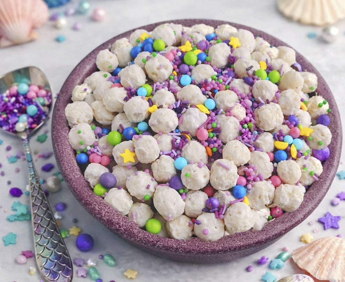 A close up of the Mermaid Poop treat in a purple bowl. There are shells and candy all around the bowl.
