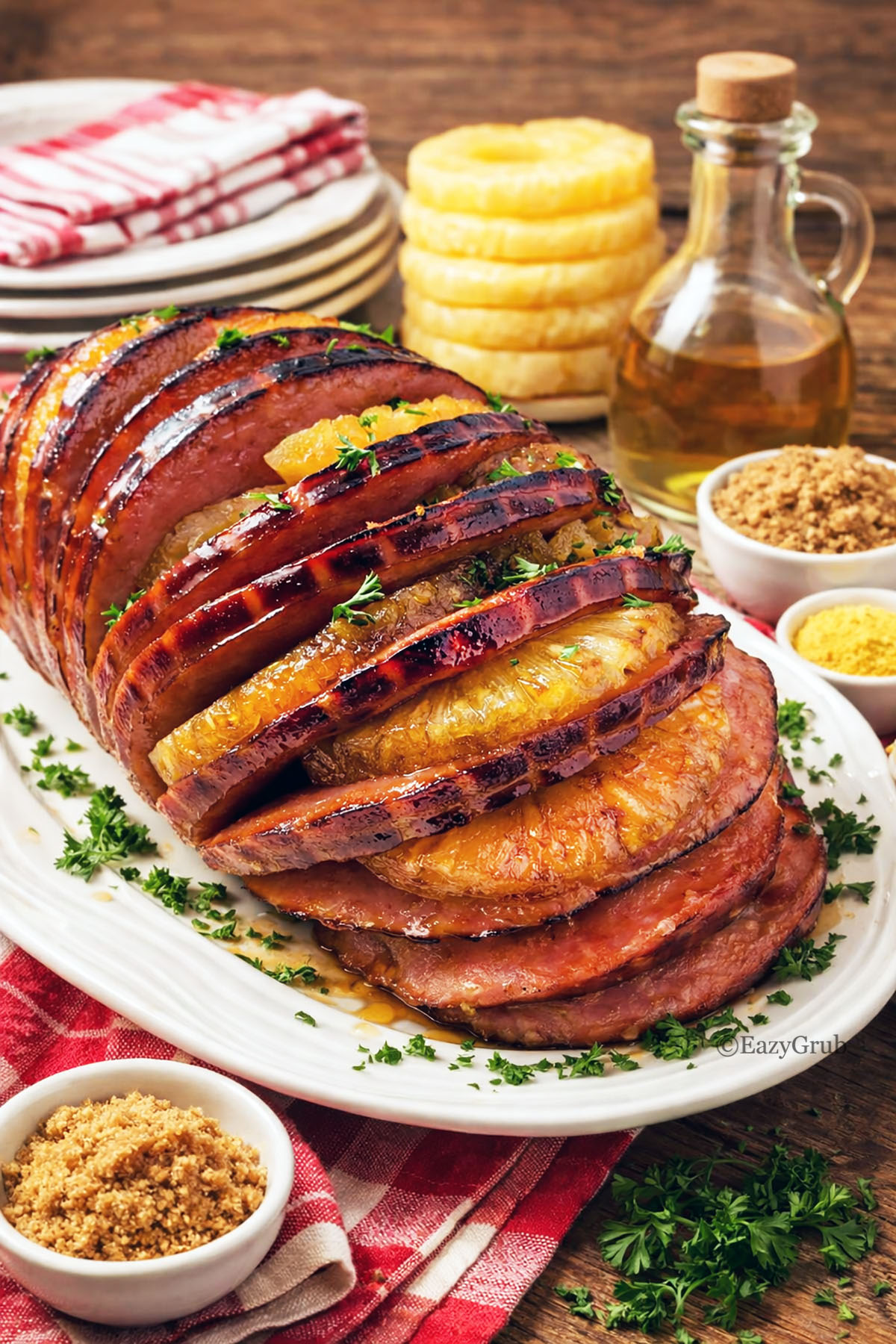 Glazed pineapple ham on a platter with garnishing items in the background.