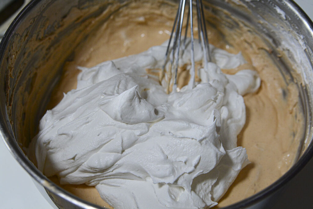 A second large dollop of whipped topping is added to the bowl, which now contains a lighter, partially aerated butterscotch mixture.