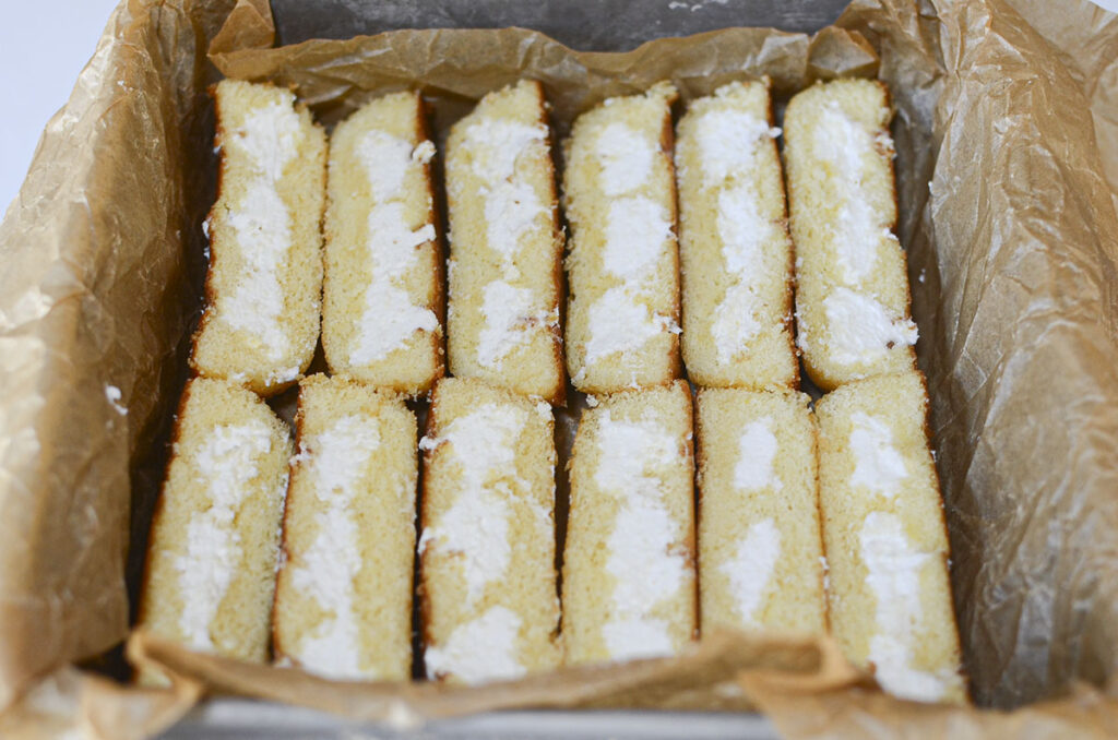 An overhead shot of packaged golden Twinkies being sliced in half lengthwise.
