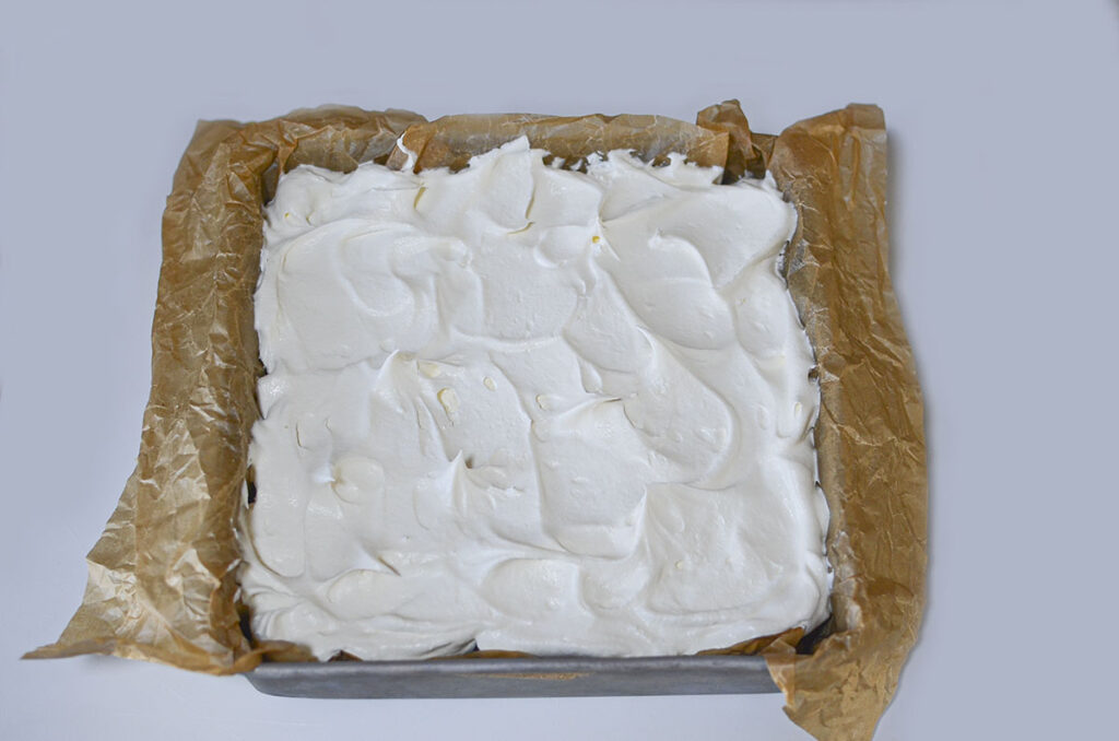 A thick, smooth layer of white whipped topping spread over the glossy red strawberry layer.