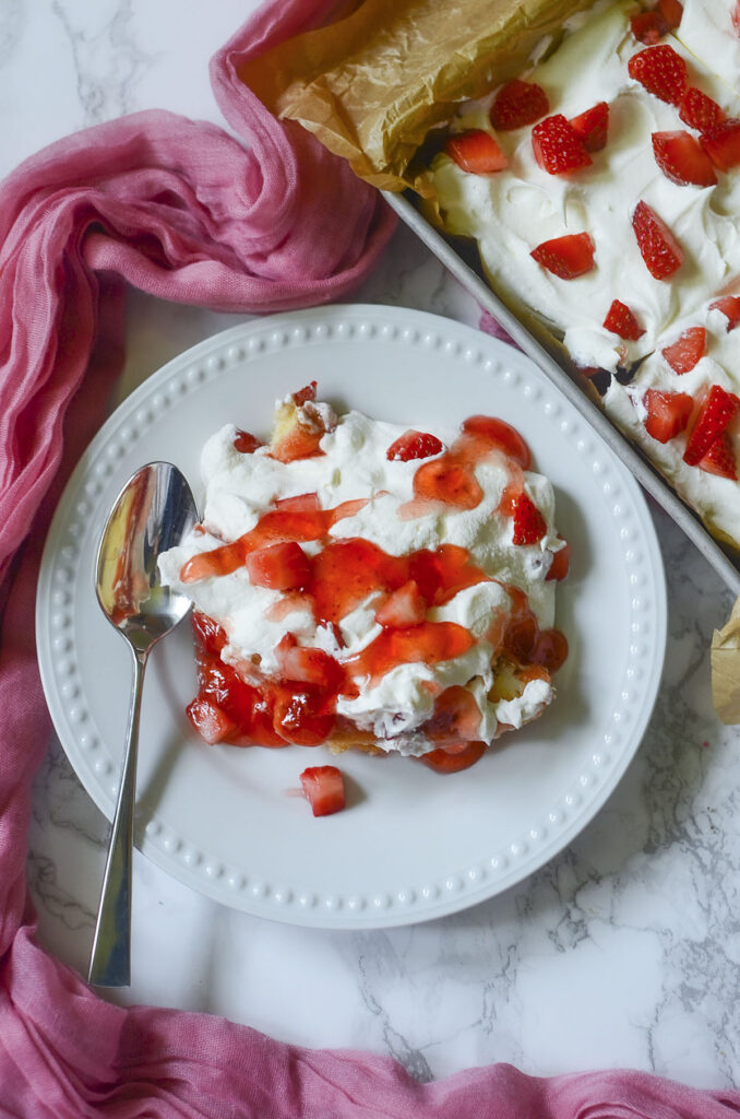 a single square slice of the Twinkie strawberry cake served on a white plate with a silver fork, cleanly showcasing the distinct layers of golden cake, red strawberry glaze, and fluffy white whipped cream.