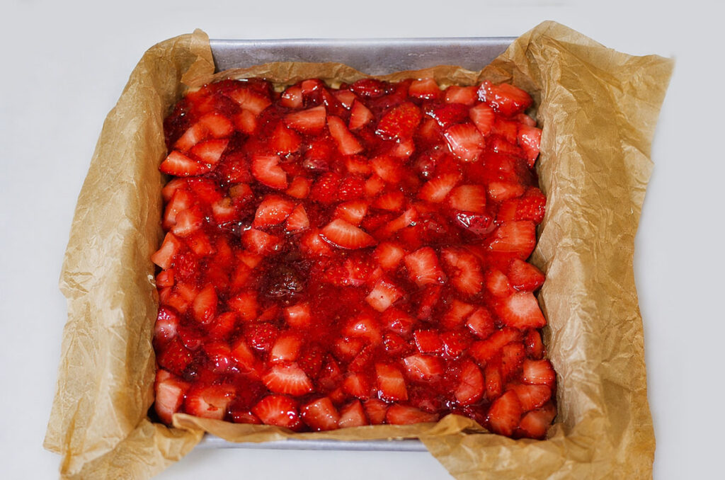 Freshly sliced strawberries mixed with vibrant red strawberry jam being spread evenly over the Twinkie layer in the baking dish.
