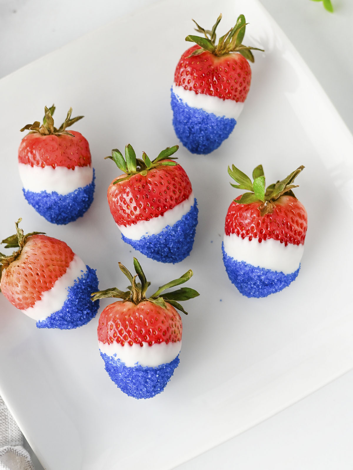 Close-up of red, white, and blue decorated strawberries sitting on a white plate.