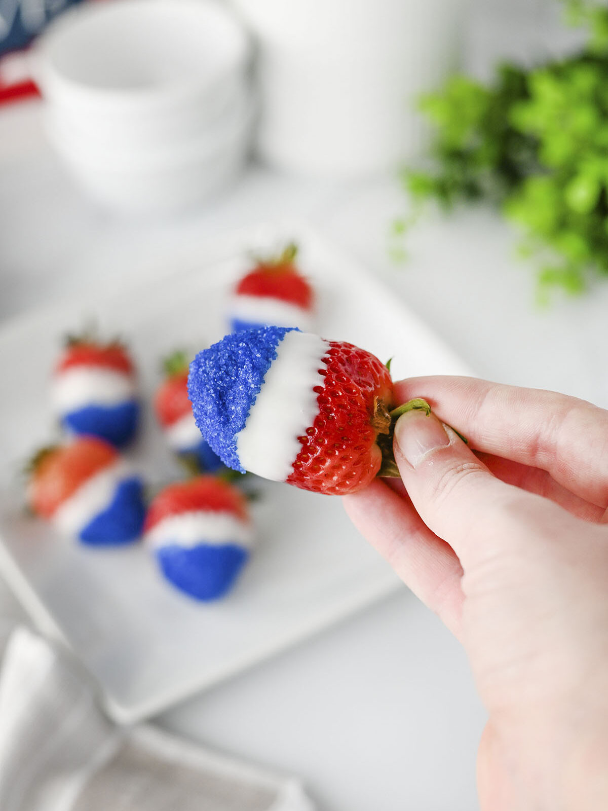 A hand holding up a completed red, white, and blue decorated strawberry.