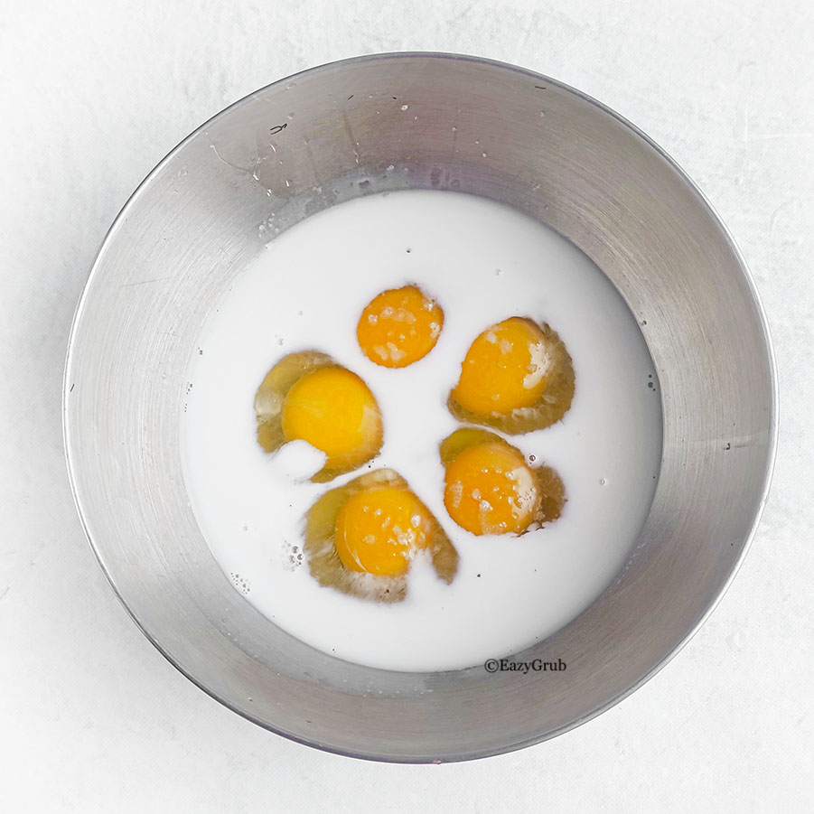 Egg yolks and milk inside a metal bowl.