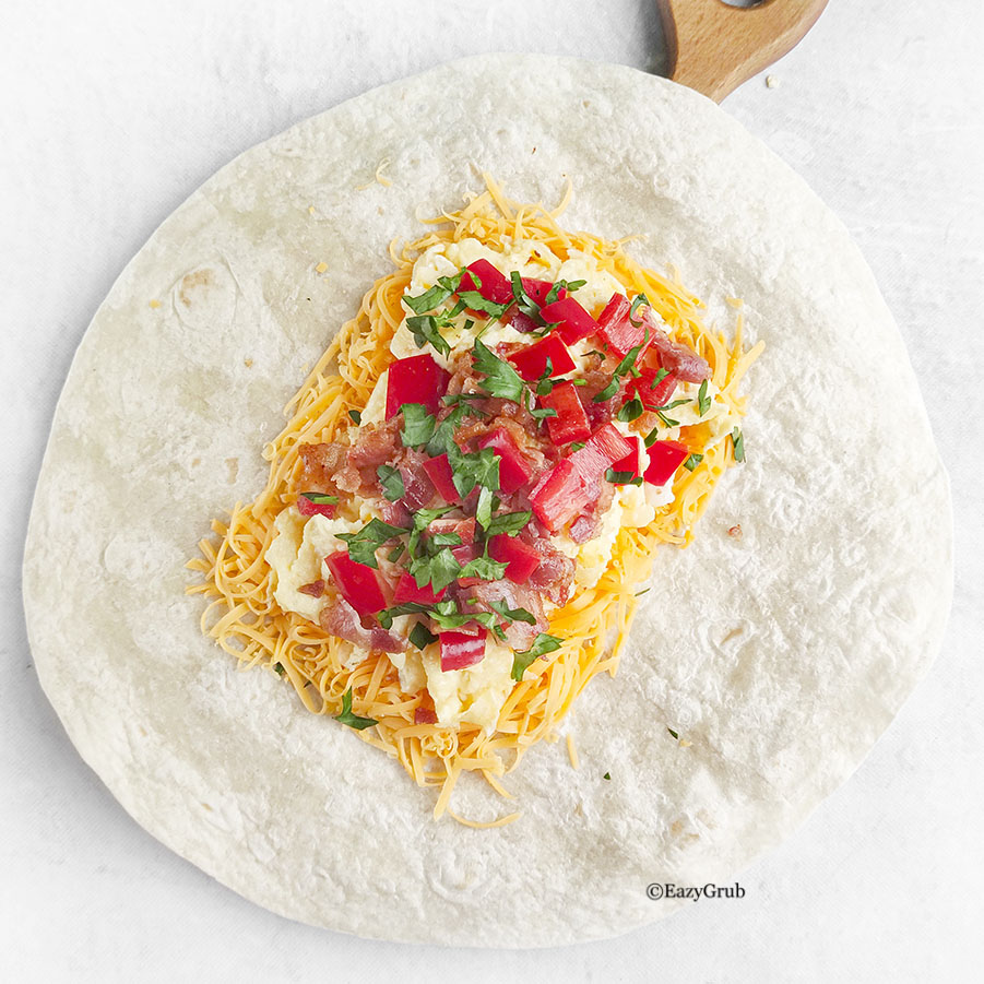 Unfolded burrito topped with scrambled eggs, shredded cheese, and herbs.