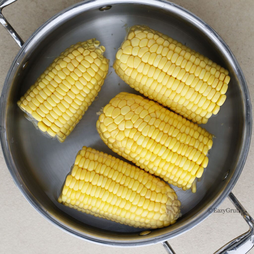 Corn cobs soaking in water inside a stainless steel pot