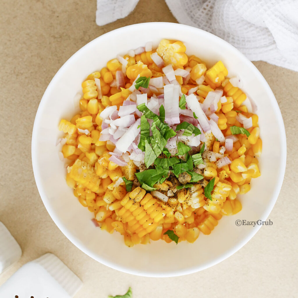 Yellow corn kernels topped with chopped red onion and fresh green herbs in a bowl.