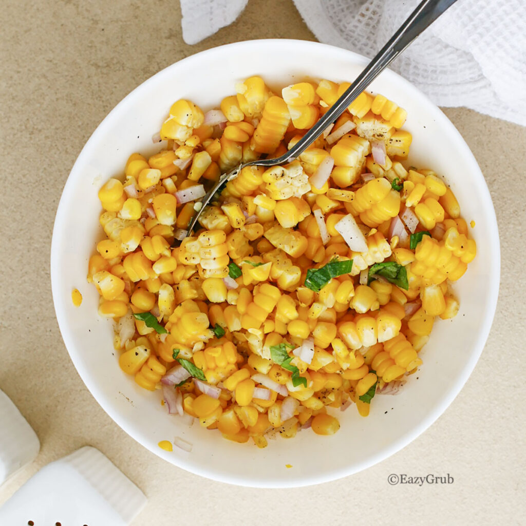 White bowl filled with yellow corn kernels mixed with diced red onion and green herbs.