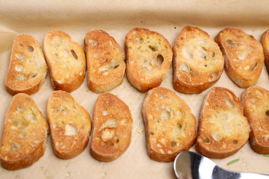 Small toasted bread slices arranged on parchment paper.