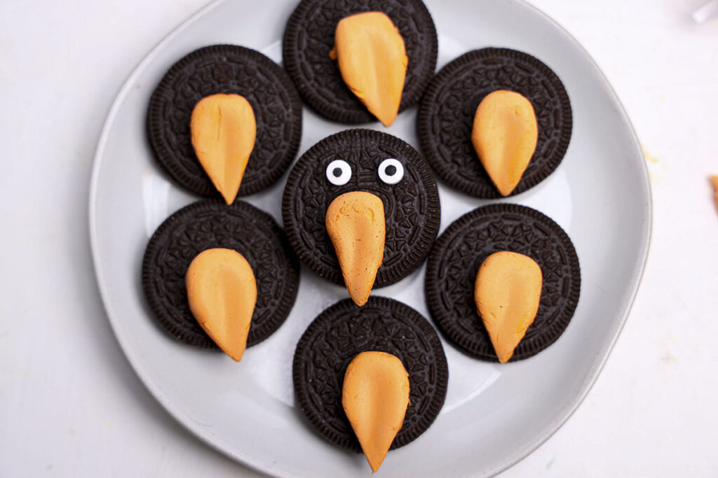 7 oreo cookies on a white plate with circus peanut noses and one cookie with eyes.