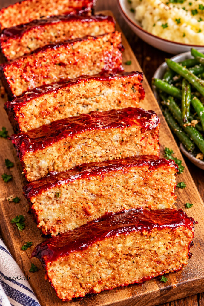 Slices of 4-ingredient stove top chicken meatloaf on a wooden cutting board with green beans on the side.