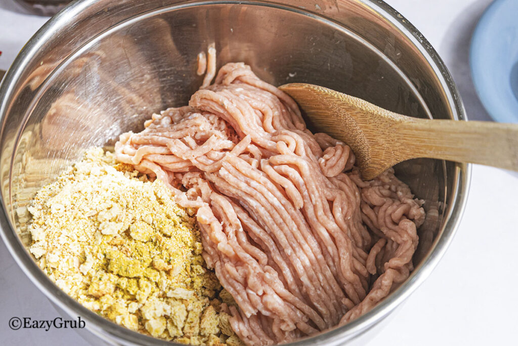 mixing the ground chicken and stuffing mixture together in a silver bowl.