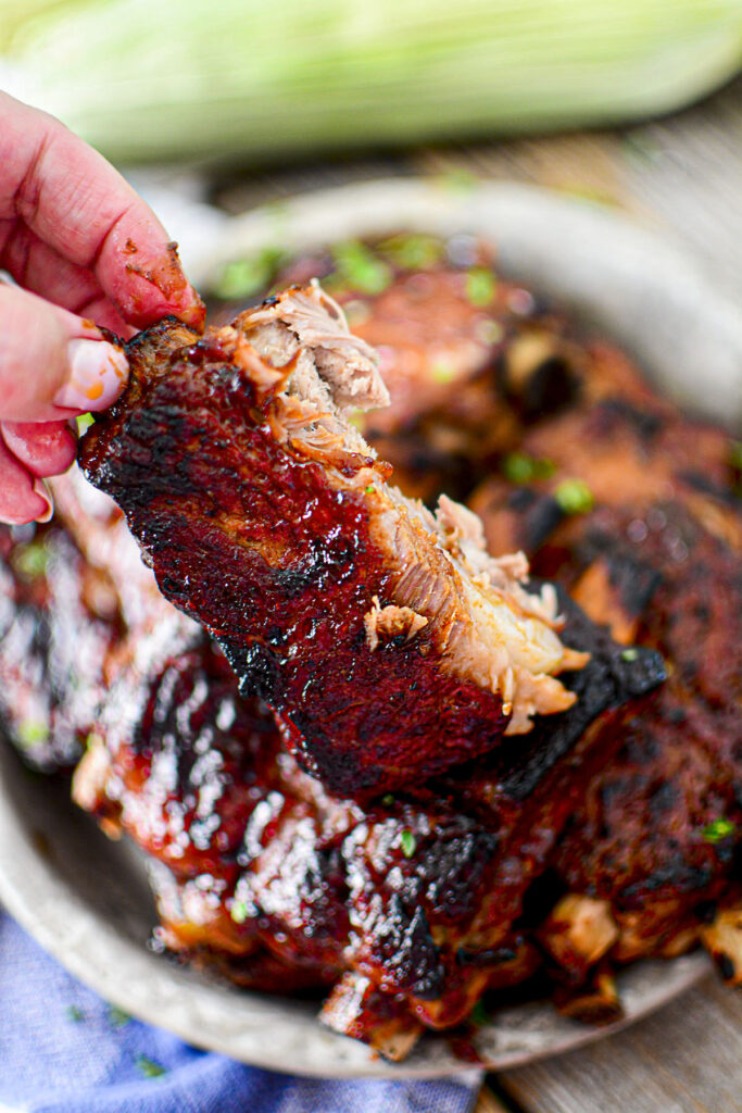 A hand holding a sauced dr. pepper rib.