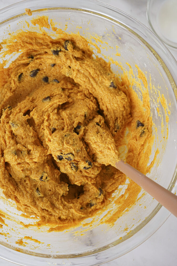 thick orange pumpkin cookie batter with chocolate chips mixed in a clear glass bowl.