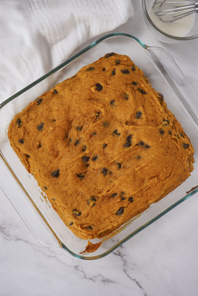 Smooth pumpkin chocolate chip bar batter spread into a square glass baking dish before baking.