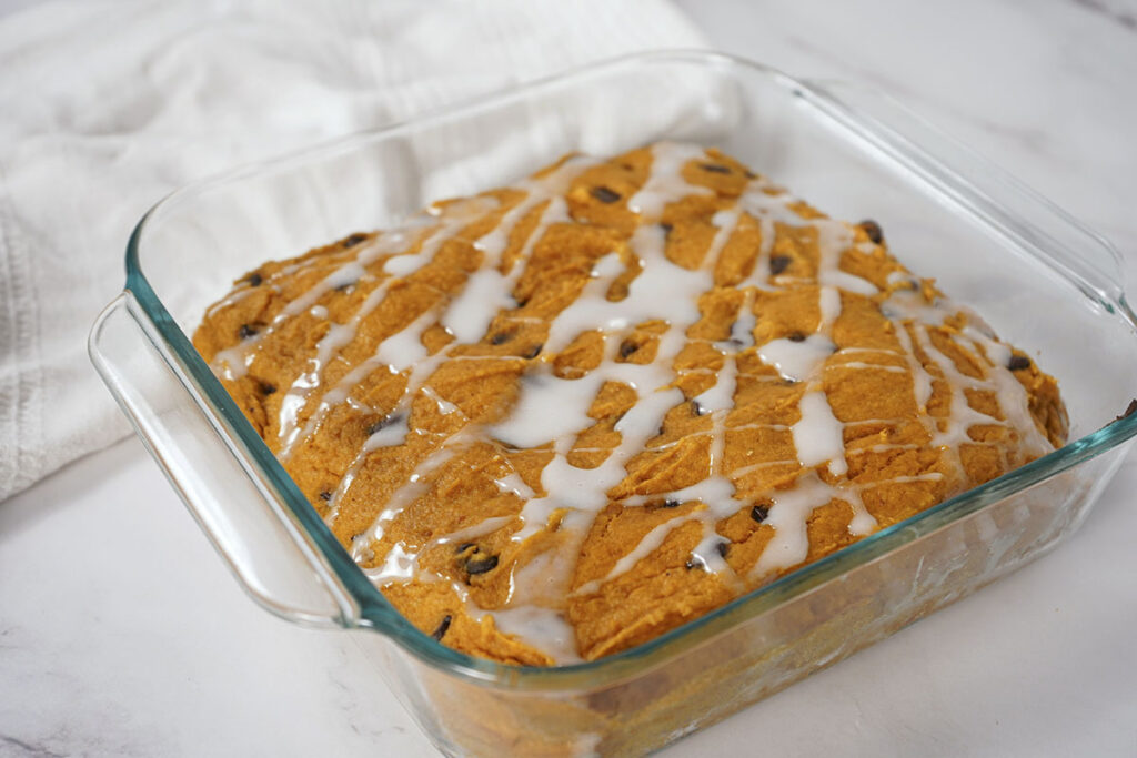 Freshly baked pumpkin bars in a glass dish drizzled with white icing icing glaze.