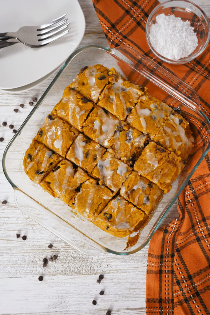 Top-down view of sliced pumpkin chocolate chip bars with white glaze drizzled on top in a square baking dish.