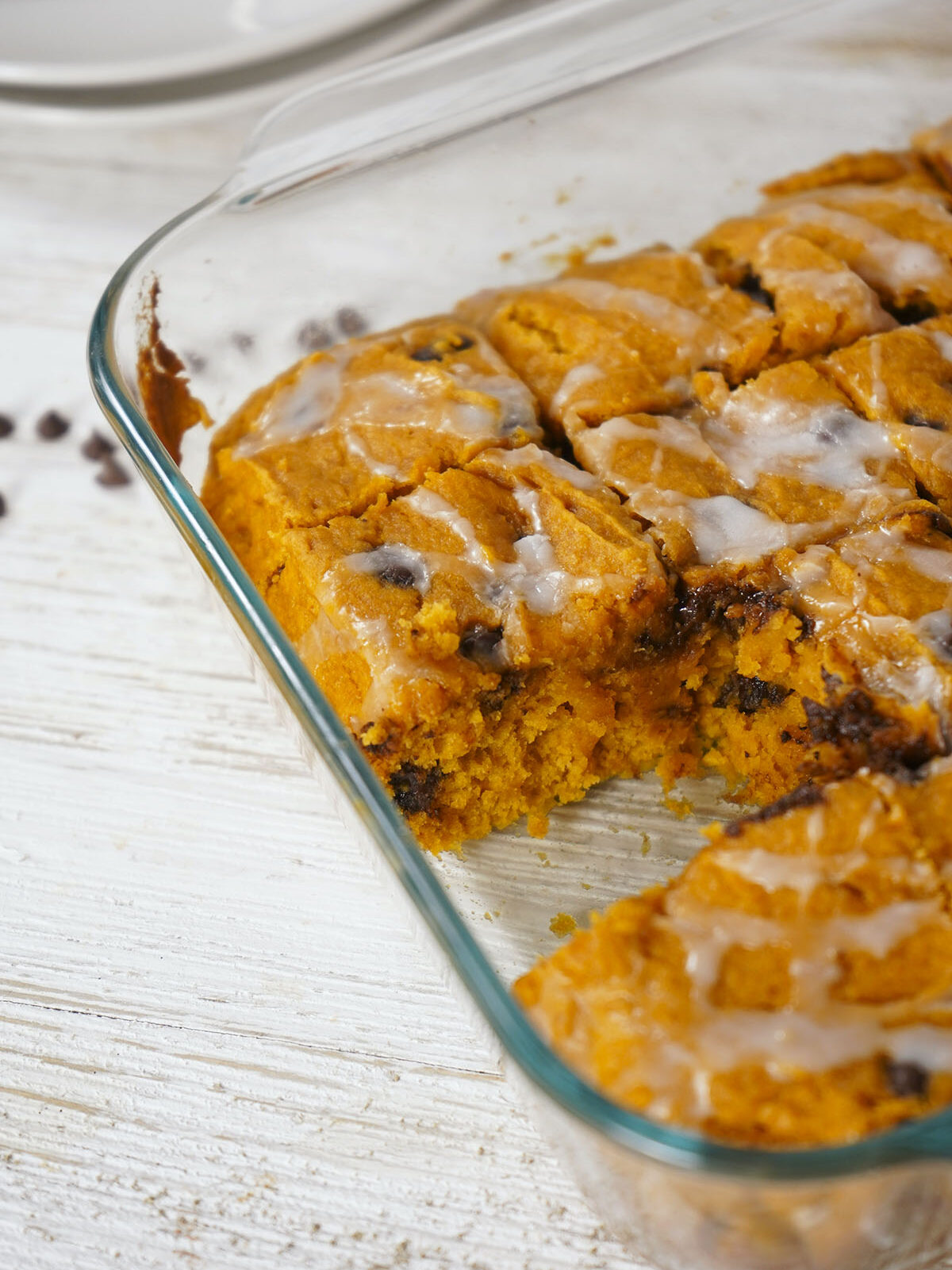 Close-up angle of iced pumpkin chocolate chip bars cut into squares in a glass baking dish.